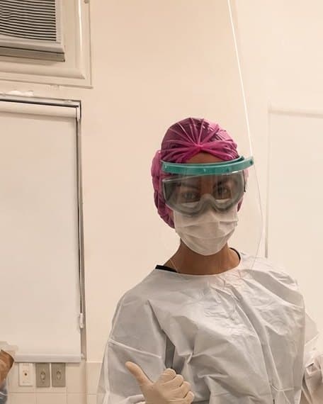 Patrícia paramentada com avental, touca, máscara e protetor facial, pronta para o procedimento.